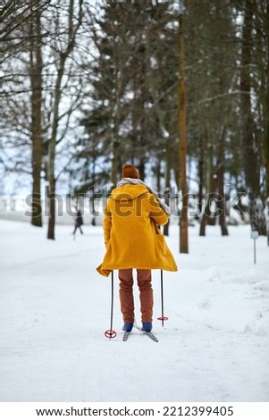Back view at young man skiing in winter forest while enjoying activity outdoors