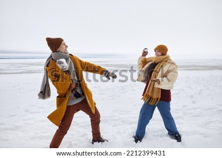Full length portrait of couple playing snowball fight outdoors in winter, copy space