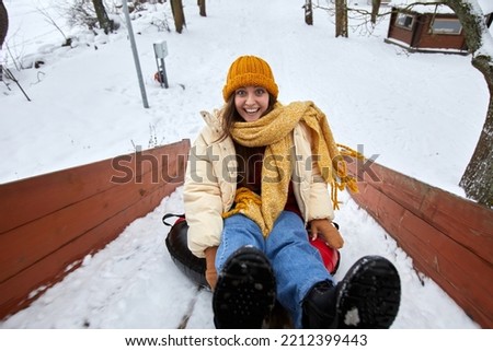 High angle portrait of excited young woman sledding downhill in winter enjoying fun outdoor activities