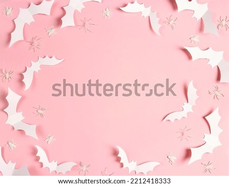 Halloween frame of white paper bats and spiders on pastel pink background. Flat lay, top view, copy space