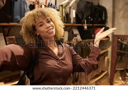 Portrait of young woman with curly hair using her smartphone to stream in shopping mall