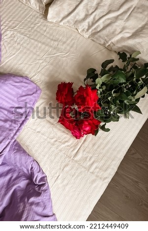 A bouquet of red roses lies on the white-lilac bed linen. Aesthetic minimalism. Greeting card with good morning.