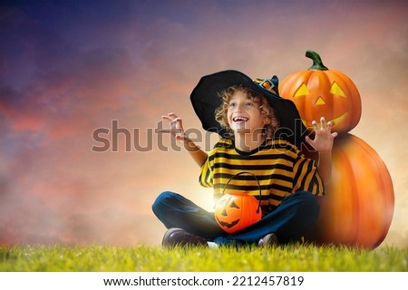 Little boy in witch costume sitting at giant pumpkin lantern on Halloween night. Kids trick or treat. Children have fun. Spooky and scary celebration. Funny curly child in black hat with candy bucket.
