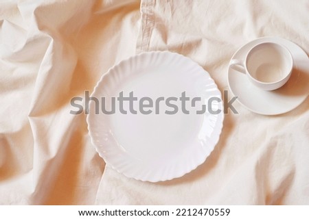 White new dishes on the table. Empty porcelain plate and small coffee cup and saucer. Flat lay photography, top view image, mockup