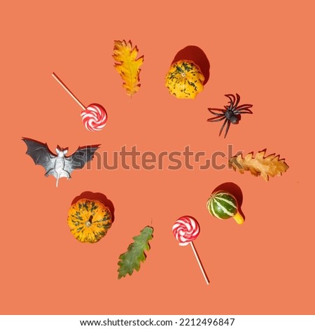 Halloween symbols composition with copy space. Little pumpkins, autumn leaves, bet, spider and candies on orange background. Minimalistic fall concept.