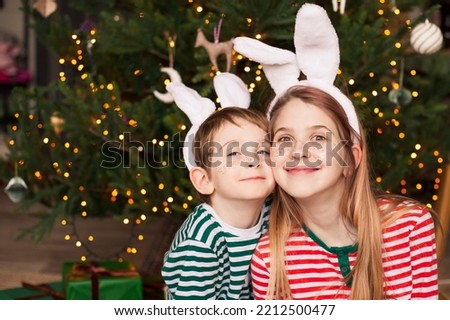 Two smiling children wearing striped pajamas and rabbit ears near christmas tree. Happy children with festive freckles tattoos waiting for the New Year of the Rabbit. Selective focus.