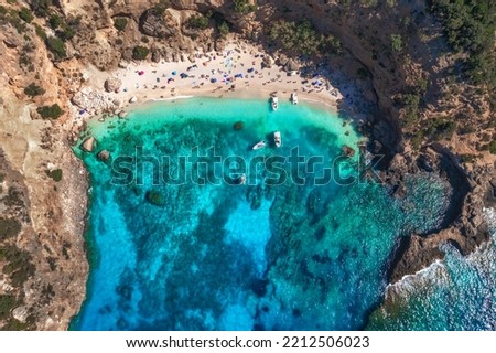 Top view of seascape with beautiful coastline and small sandy beach with colorful umbrellas. Sea coast with blue, turquoise clear water on a sunny day, aerial drone shot 