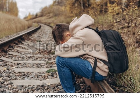 Sad teenager boy with backpack sitting on rails of railway. Mental health concept. Royalty-Free Stock Photo #2212515795