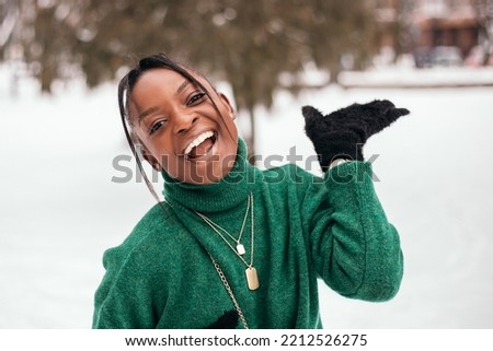 African american woman standing street outside with white snow background, dressed warm green sweater, smiling, looking aside. New Year atmosphere, winter vacation, cold weather