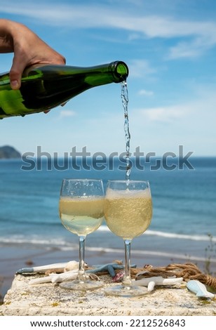 Pouring of txakoli or chacolí slightly sparkling very dry white wine produced in Spanish Basque Country, served outdoor with view on Bay of Biscay, Atlantic Ocean. Royalty-Free Stock Photo #2212526843
