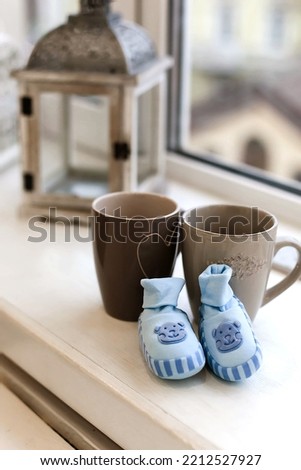Small baby shoes and cups of warm tea, child waiting concept