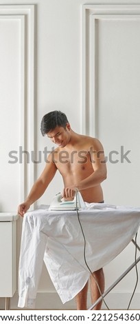 Man is ironing in the bath room, washing and dryer machine in front of the white and brown vertical wall style.