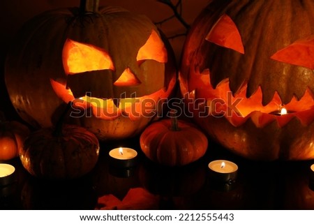 Carved Halloween pumpkins and burning candles on dark background, closeup