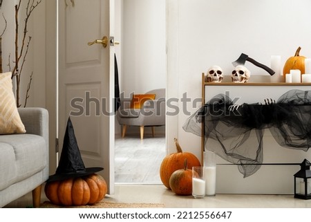 Interior of modern living room with chest of drawers, open door and Halloween decor