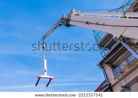 Construction crane boom with a load feeder against the backdrop of a house under construction.