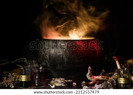 Witch's cauldron with potion and different magic attributes for ritual on dark background Royalty-Free Stock Photo #2212557479