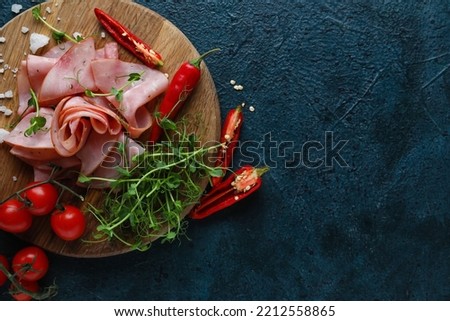 Wooden board with slices of tasty ham, vegetables and microgreen on dark color background