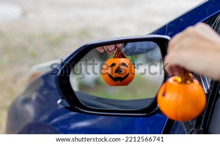 smiling plastic halloween pumpkin mini small pumpkin in reflection rear view retractable lateral mirror.woman hand holding pumpkin bucket handle.trick or treat holiday, car auto vehicle vehicle part