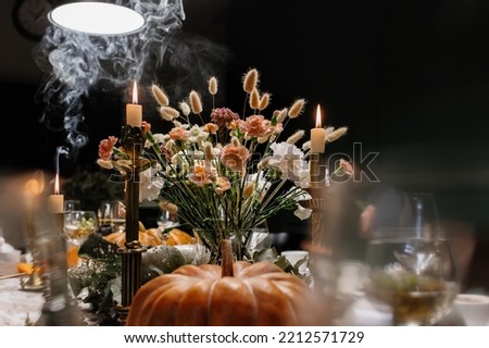 The Thanksgiving dinner table. A traditional Thanksgiving or Friendship Day party. Decoration and serving of the festive table with autumn decor, candles and flowers dishes and pumpkins.