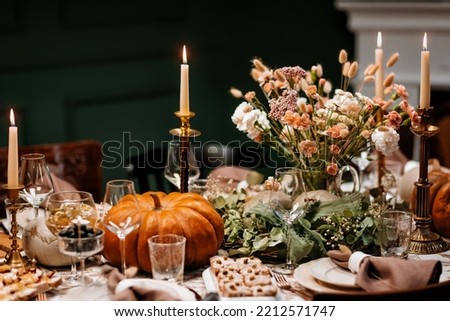 The Thanksgiving dinner table. A traditional Thanksgiving or Friendship Day party. Decoration and serving of the festive table with autumn decor, candles and flowers dishes and pumpkins. Royalty-Free Stock Photo #2212571747