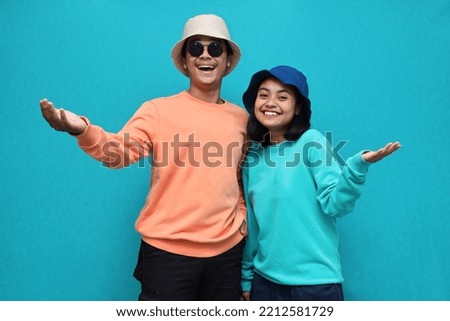 Portrait of happy cheerful awesome Asian couple with big smiles opening hands on isolated light blue background