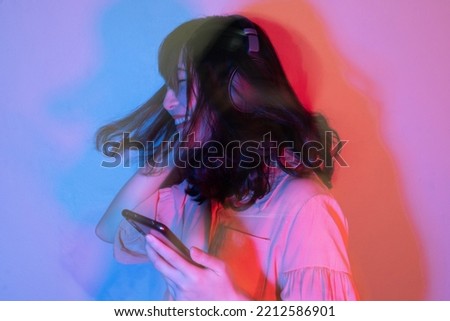Happy Asian​ woman​ in headphones using smartphone for listening​​ to music​ and​ dancing with hair moving on neon light background. Motion Blur.