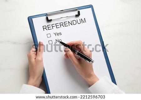 Woman with referendum ballot making decision at white marble table, closeup Royalty-Free Stock Photo #2212596703
