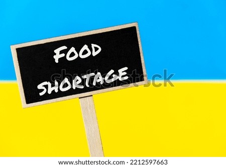 Wooden information label sign with text FOOD SHORTAGE against Ukrainian national flag message. Global hunger, inflation, high prices, increasing living expenses and poverty, financial crisis, food