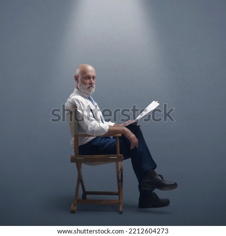 Professional filmmaker sitting on the director's chair and holding a screenplay, he is looking at camera Royalty-Free Stock Photo #2212604273