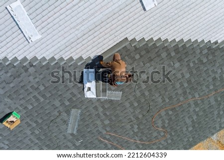 Worker uses an air hammer to nail new shingles bitumen for roof using top view from above Royalty-Free Stock Photo #2212604339