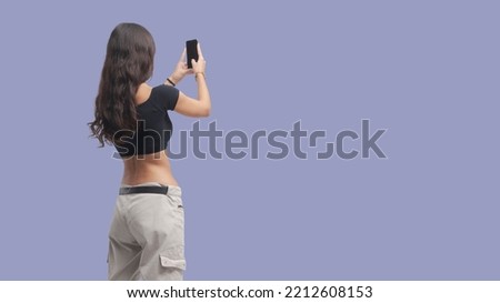 Young beautiful woman taking pictures with her smartphone, back view, copy space