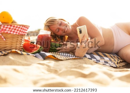 Cheerful young woman enjoy at tropical sand beach. Young woman taking a picture of fruit on the beach.	