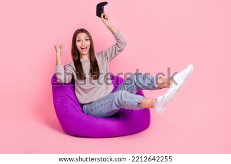 Full size photo of delighted girl sit cozy bag hold controller raise fist achievement isolated on pink color background