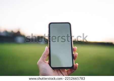 Selective focus of hand of crop person taking picture of blurred green park on smartphone with blank screen in summertime