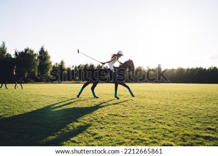 Side view of unrecognizable female jockey riding horse and playing Polo on green meadow against cloudless sky during training in summer Royalty-Free Stock Photo #2212665861