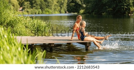 mother and daughter bathing and splashing water with their foot at jetty on a lake in summer Royalty-Free Stock Photo #2212683543