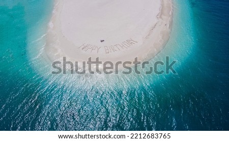 Hand written Happy Birthday on the sandy beach by the ocean on a desert island. Shooting from the air with a copter