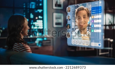 Young Woman Using Augmented Reality Software At Home, Sitting on a Couch in Living Room, Making Gestures to Answer AR Video Call Chat with Friends, Family. Female Talking on Online Meeting.
