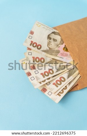 A stash of money in 100-hryvnia banknotes coming out of an envelope on a blue background. Selective focus, noise. The concept of salary, bribe, credit, debt, profit