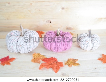 beige and soft pink colored crochet woolen pumpkins on wooden ground with autum leaves