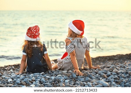 two girls sisters in santa claus hats have fun on the seashore at sunset 