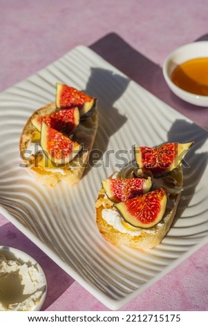 Open sandwiches or bruschetta with cream cheese, fresh figs, honey and walnuts on a white rectangular plate on a pink concrete background. Italian food