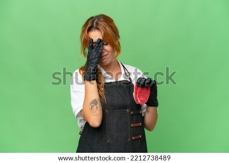 Butcher caucasian woman wearing an apron and serving fresh cut meat isolated on green screen chroma key background with tired and sick expression