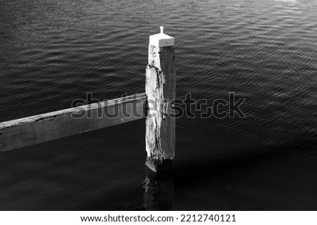 Black and white picture of a wooden post in calm water. Pole standing in water. Small waves around a steady pole in the water. Symbol of consistency and strength or power. Slide background symbol 
