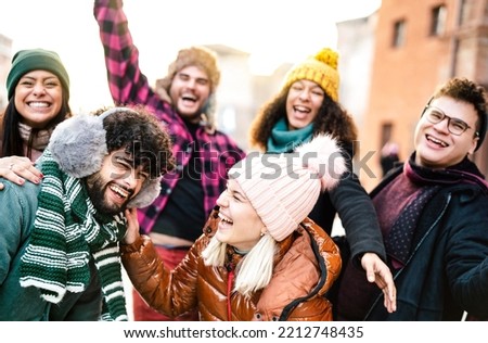 International guys and girls taking funny face selfie wearing warm fashion clothes - Happy life style concept with milenial people having fun together outside on winter holidays - Warm sunshine filter Royalty-Free Stock Photo #2212748435