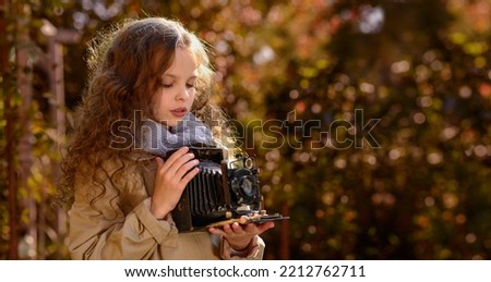 Portrait of young beautiful child with retro camera. Little girl with old photography camera in hands outdoors. Child hobby and  education. Kid and photography. Selective focus, close up.