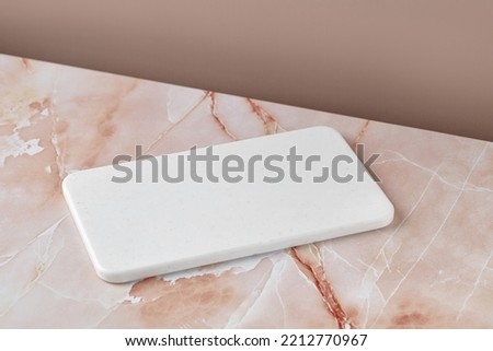 Empty blank white cutting board on beige pink marble background. Minimalist mock up for product presentation.
