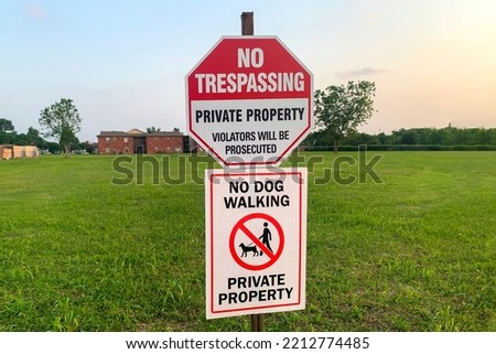 The prohibitive sign on the label No trespassing, private property, violators will be prosecuted, no dog walking against the green lawn in sunlight.
