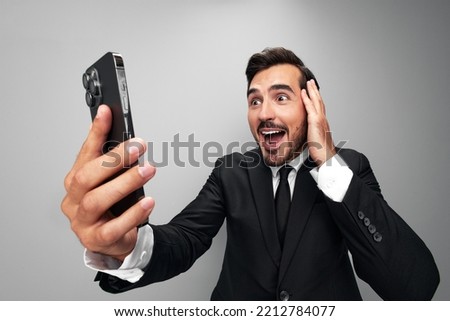 Man businessman holding phone in hand surprised looking at screen video call and selfies and smile with teeth. Close-up wide angle photo gray isolated background