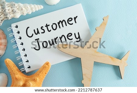 Top view of notepad written with CUSTOMER JOURNEY text on blue background with airplane figurine and seashells